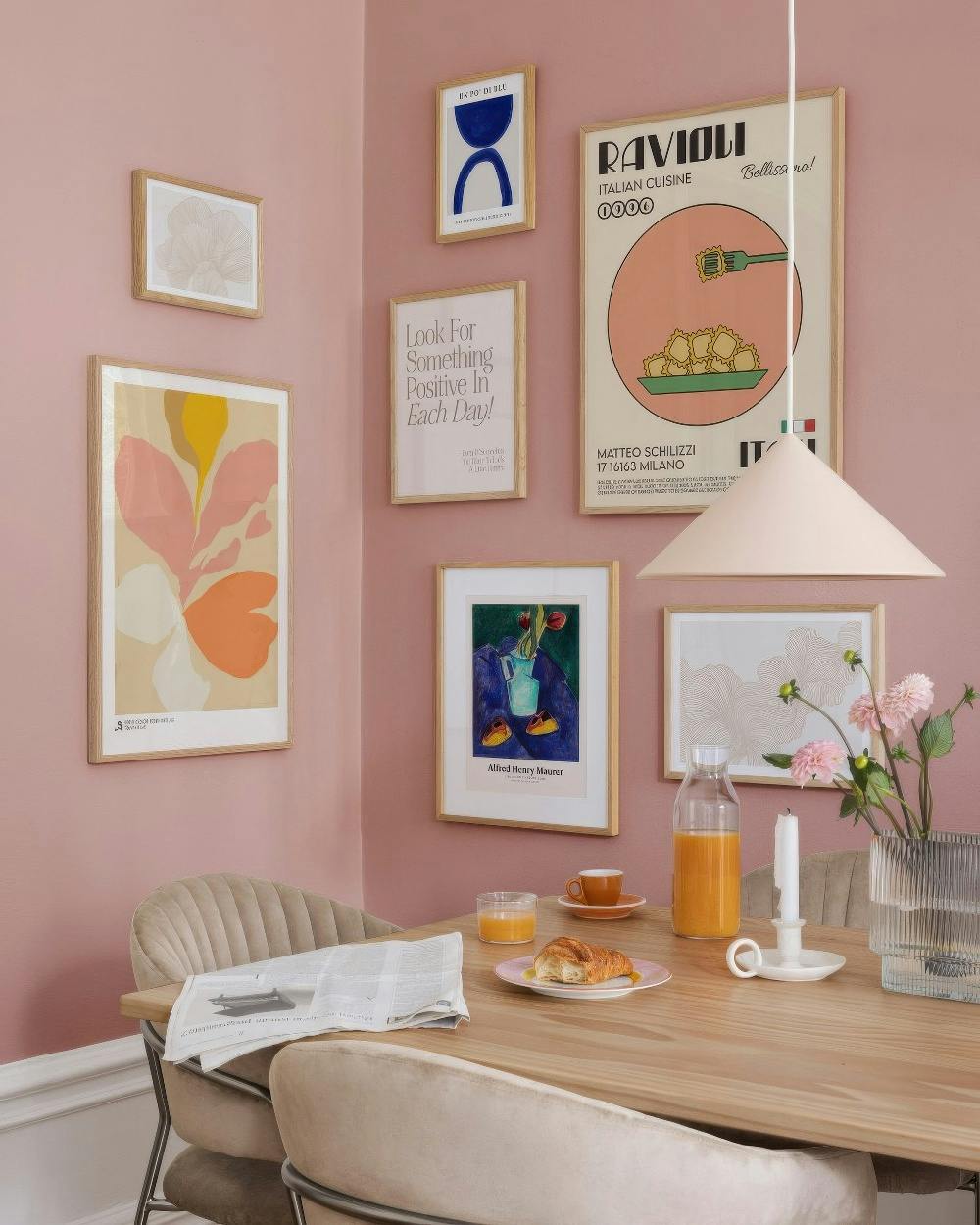 Galleria a parete con stampe astratte, floreali, un poster di ravioli e una citazione motivazionale su una parete rosa.