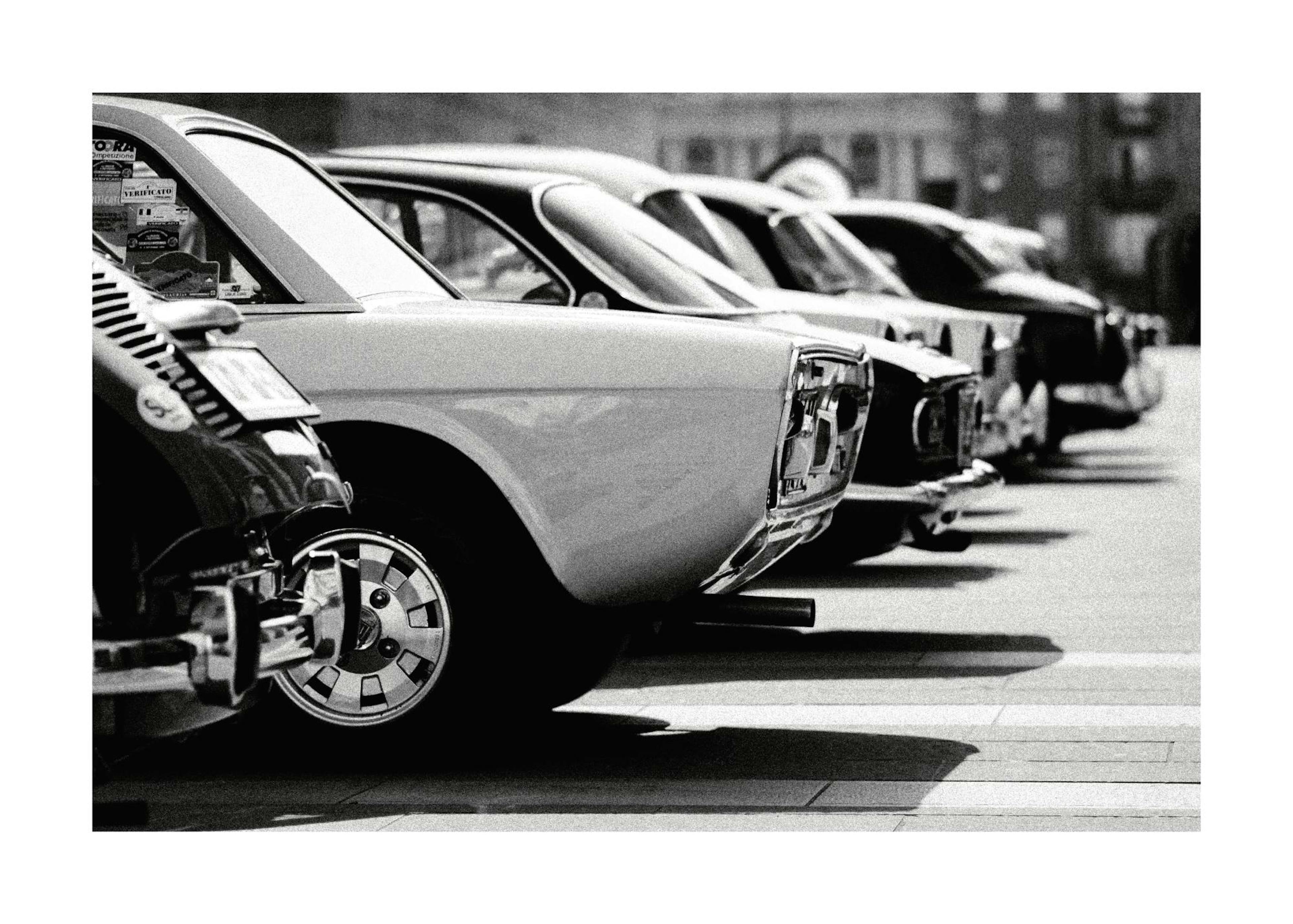 Fotografia in bianco e nero di una fila di auto depoca retrò parcheggiate, con bordi bianchi.