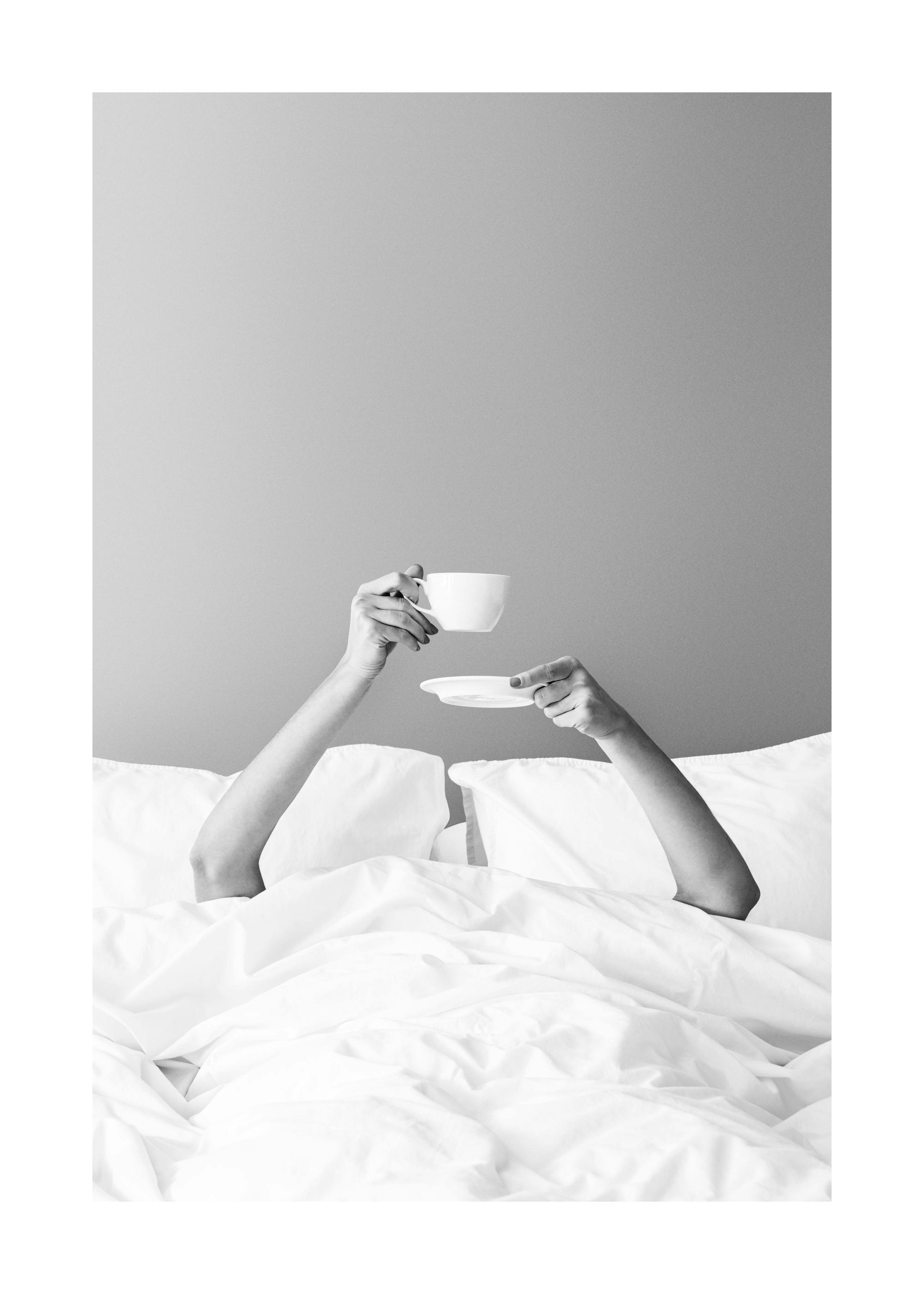 Black and white photograph of a person in bed holding a coffee cup and saucer, a breakfast in bed poster print.