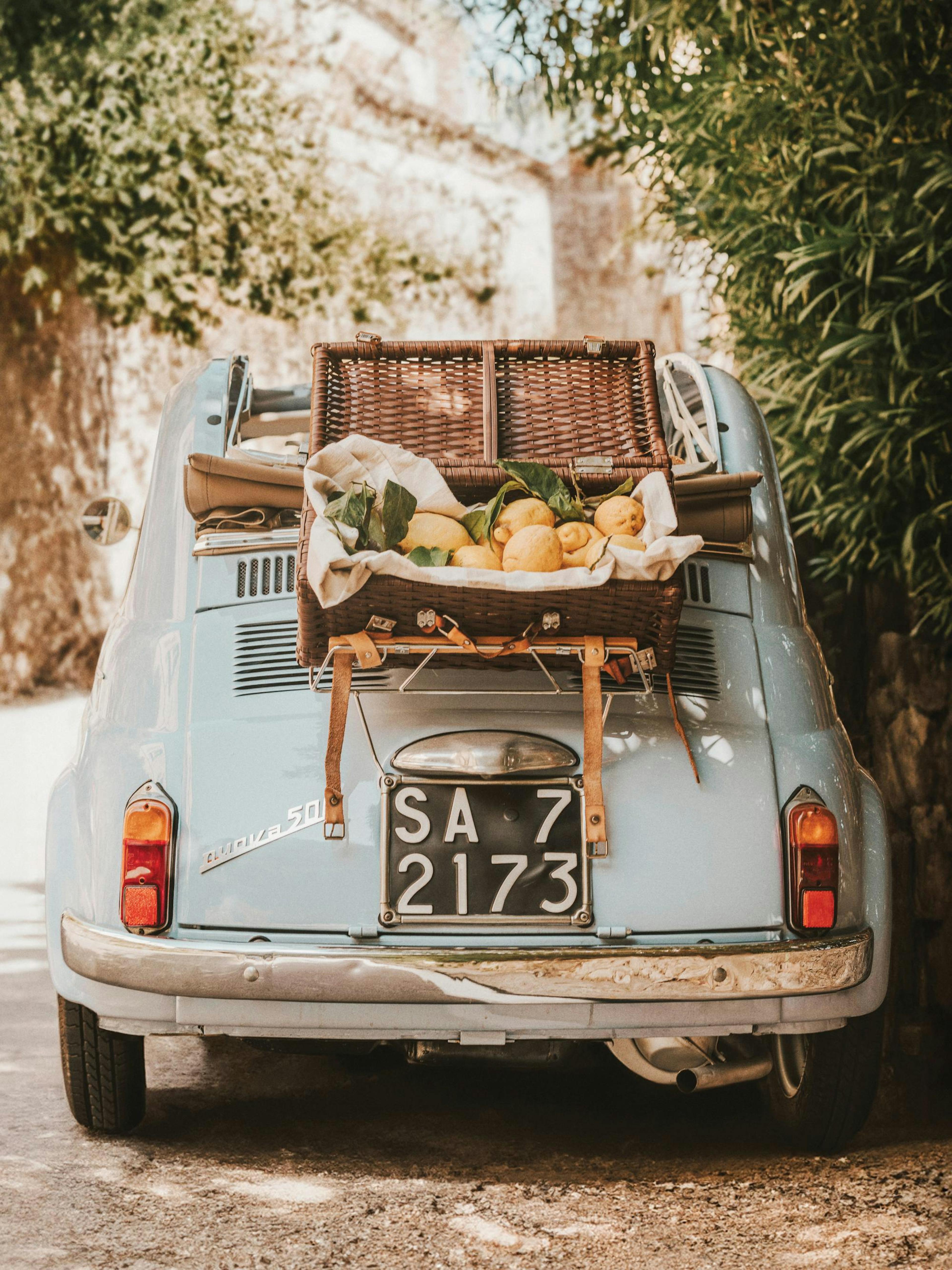 レモンとピクニックバスケットを積んだヴィンテージの淡い青色の車が写ったノスタルジックな写真プリント